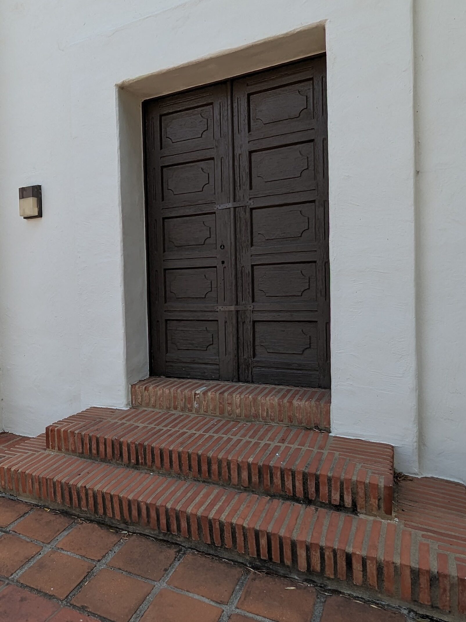 Ornate Mission Style Door against white plaster door structure, with terracotta brick floor and step at entrance.